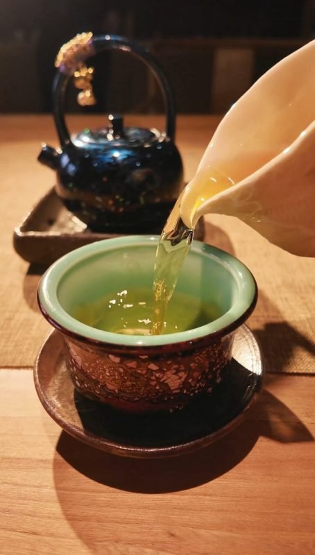Handmade lacquer tea cup beside warm tea in soft shadow