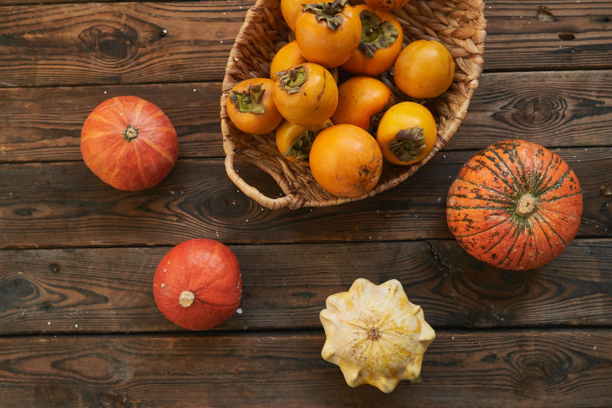 Autumn harvest of pumpkins, persimmons, grains, and seasonal produce arranged in a woven basket