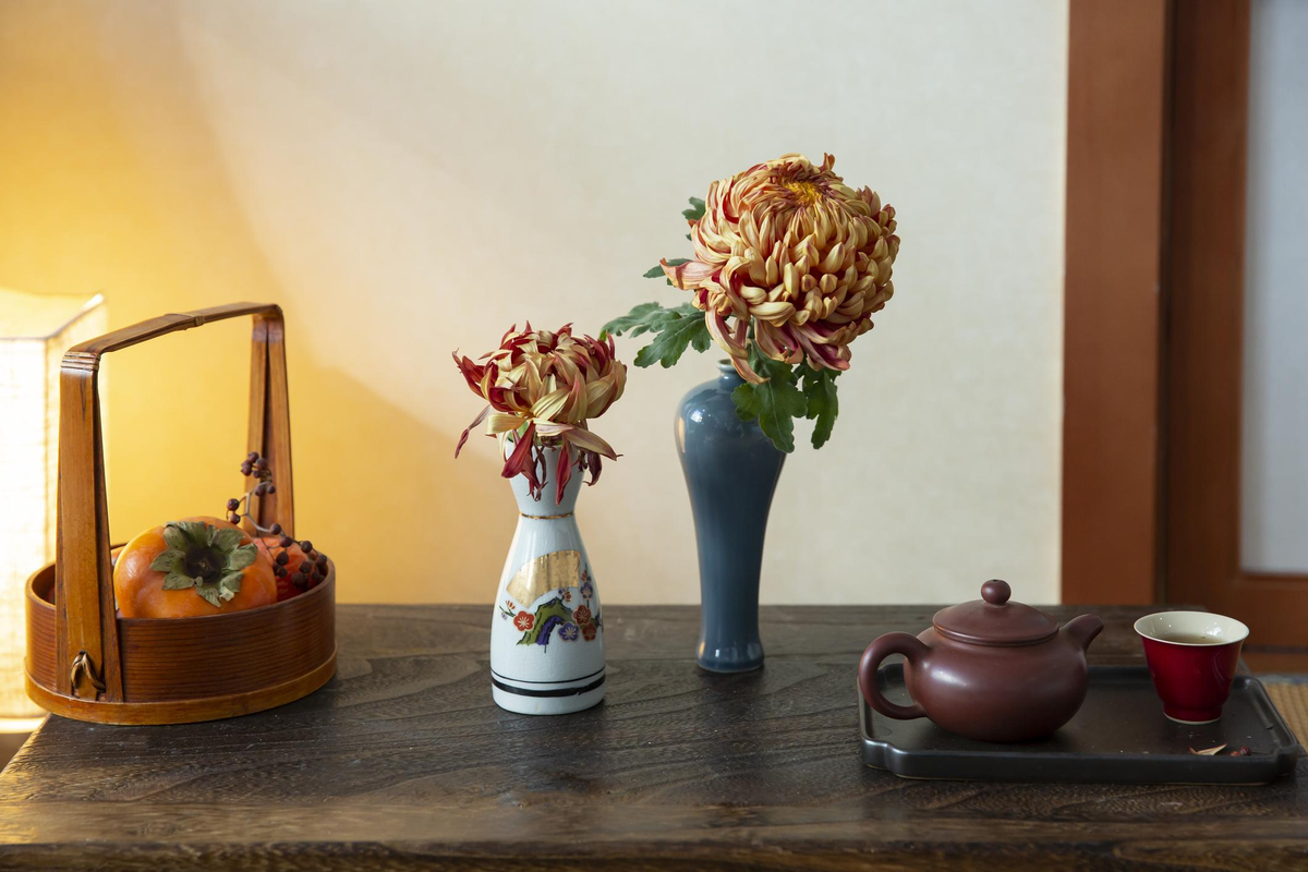 Handmade ceramic teacup, black lacquerware tea container, and autumn chrysanthemums arranged on a wooden tea tray