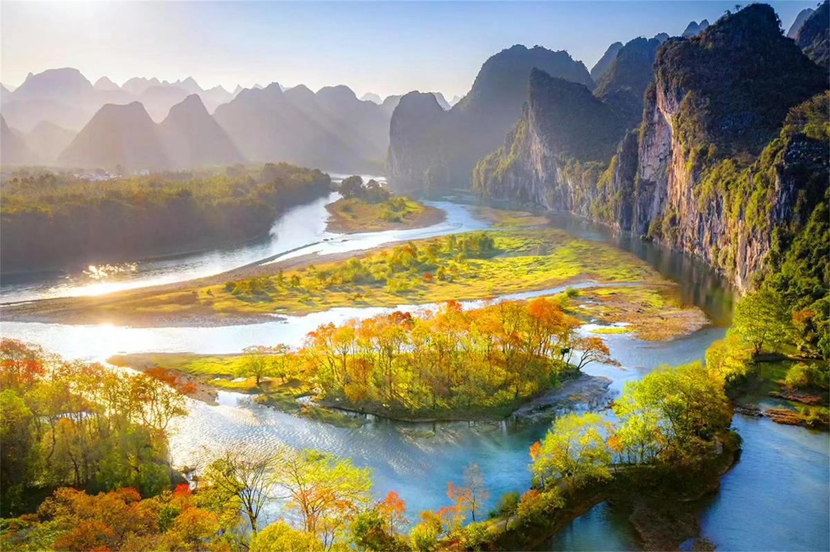 Layered autumn mountains and a winding river covered in morning mist beneath a soft golden sky